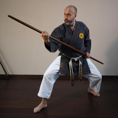 Thierry MICHEL, disciple dévoué de Sensei Chinen, est capturé dans une posture de blocage symbolique avec le Bô, le bâton traditionnel d'Okinawa. Sa concentration et sa détermination transparaissent dans chaque détail de sa posture. L'angle de la photo met en valeur la longueur du Bô et la technique précise de Thierry. L'arrière-plan est flou, mettant l'accent sur sa silhouette déterminée, un hommage vivant à l'héritage martial d'Okinawa.