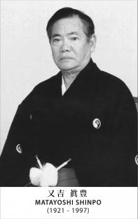 Portrait solennel de Sensei Shimpo Matayoshi, vêtu de son habit de cérémonie traditionnel. Son regard est profond et empreint de sagesse, reflétant des années de dévouement et de maîtrise dans les arts martiaux. L'arrière-plan est neutre, mettant en valeur la stature imposante et le charisme de Sensei Matayoshi.